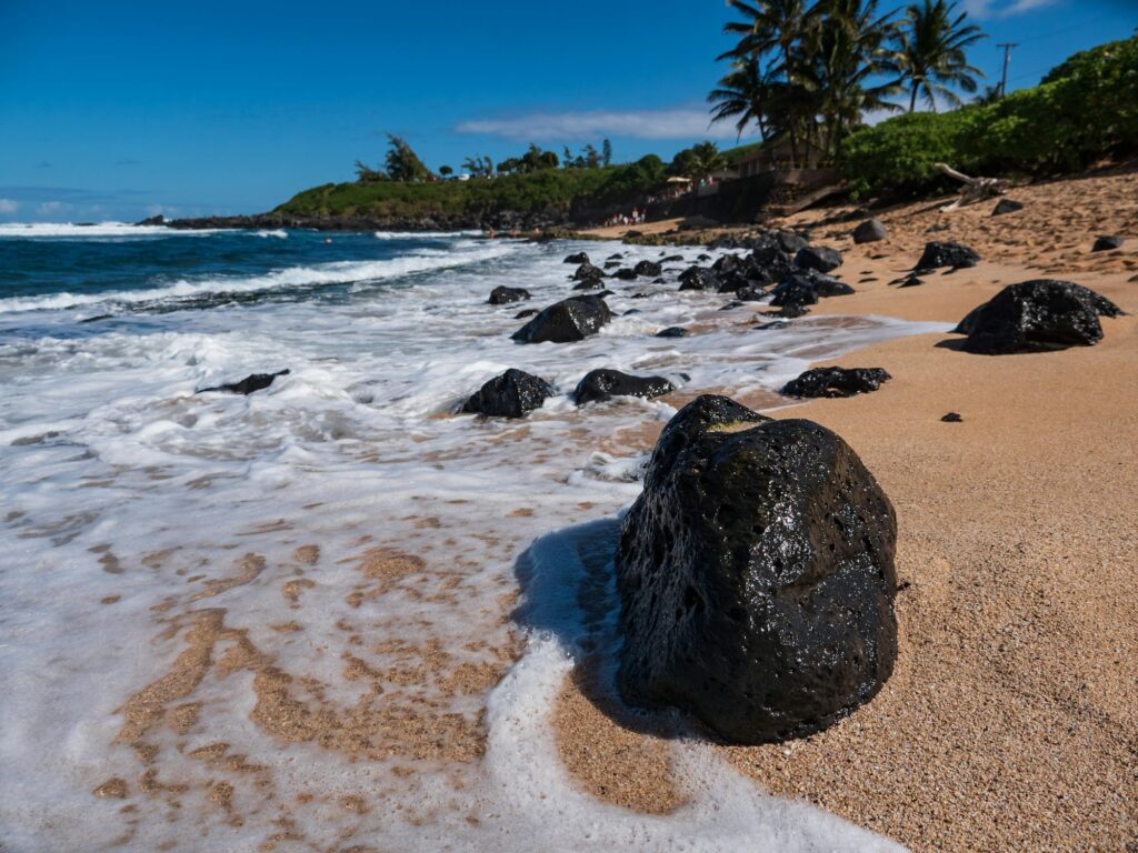 A black lava rock in front of the camera that is laying on Maui's Beach seashore
