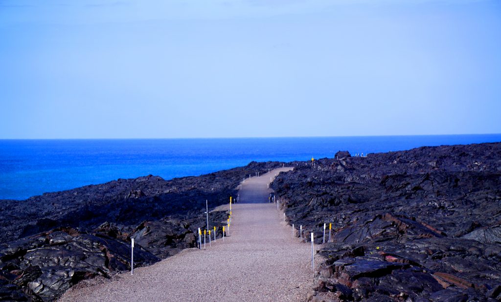 A pathway with lava rocks surrounding it and an ocean view on Hawaii Volcanoes National Park is on Hawaii Island (the Big Island).