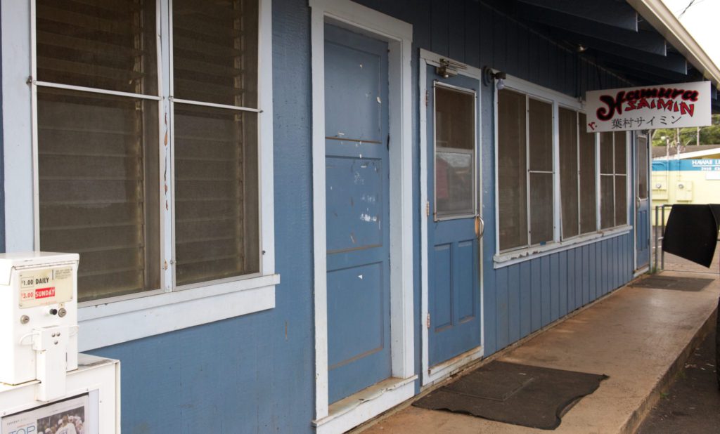 A perspective view of a blue building with the hanging sign saying Hamura Saimin, a restaurant in Lihue that is in southeastern Kaua'i, 