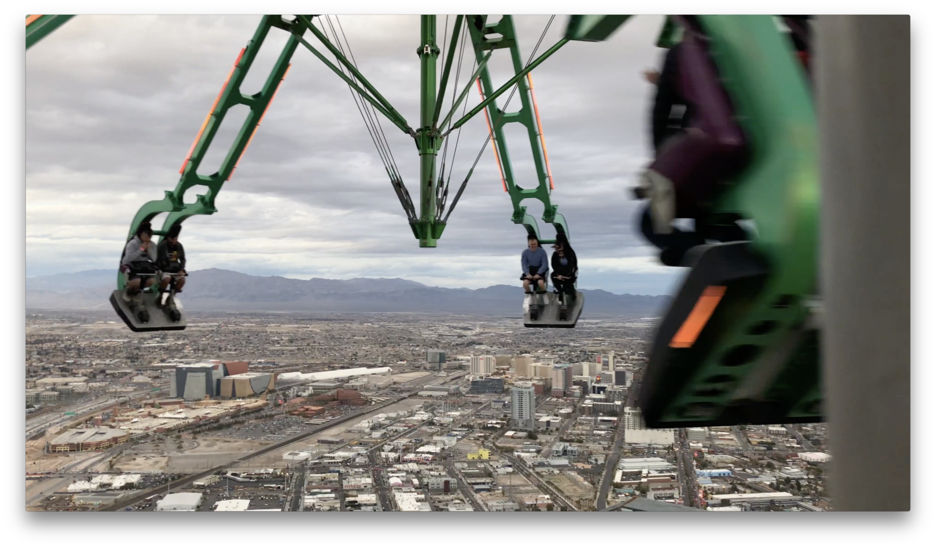 The Strat Casino Skypod in motion as it's swinging it's riders with its towering structure ascending into the sky amidst a backdrop of the Las Vegas city building and towers