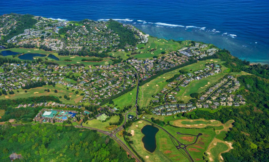 Aerial view of Princeville, Hawaii, presenting green nature cliffs cascading down to pristine beaches, framed by the azure waters of the Pacific Ocean.