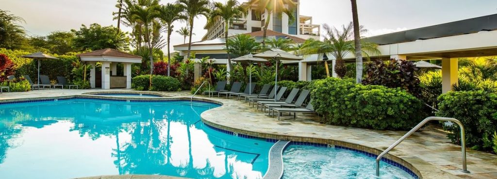 Close up of Maui Coast Hotel's pool with chairs line up on the side and the building in the background