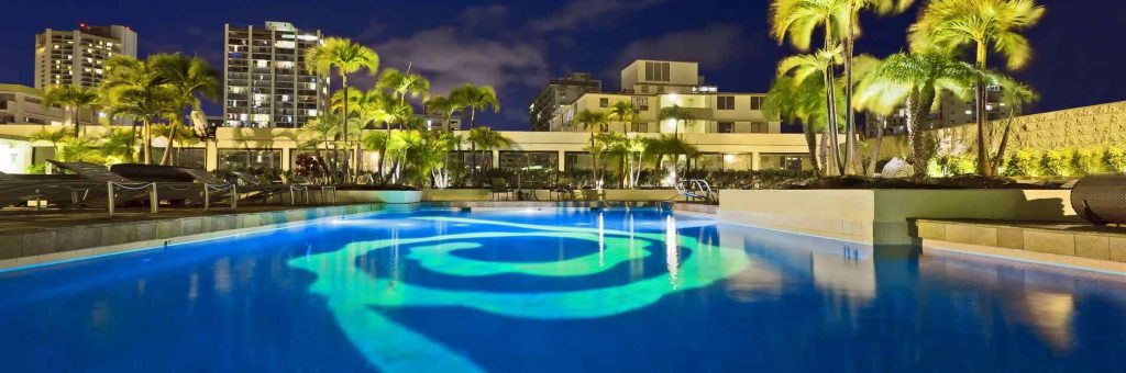 Hilton Waikiki Beach pool at night where you can see the lights glowing through the water