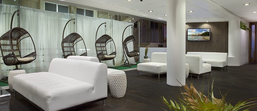 Stay Hotel Waikik lobby of white sofas, hanging rattan chair, and TV