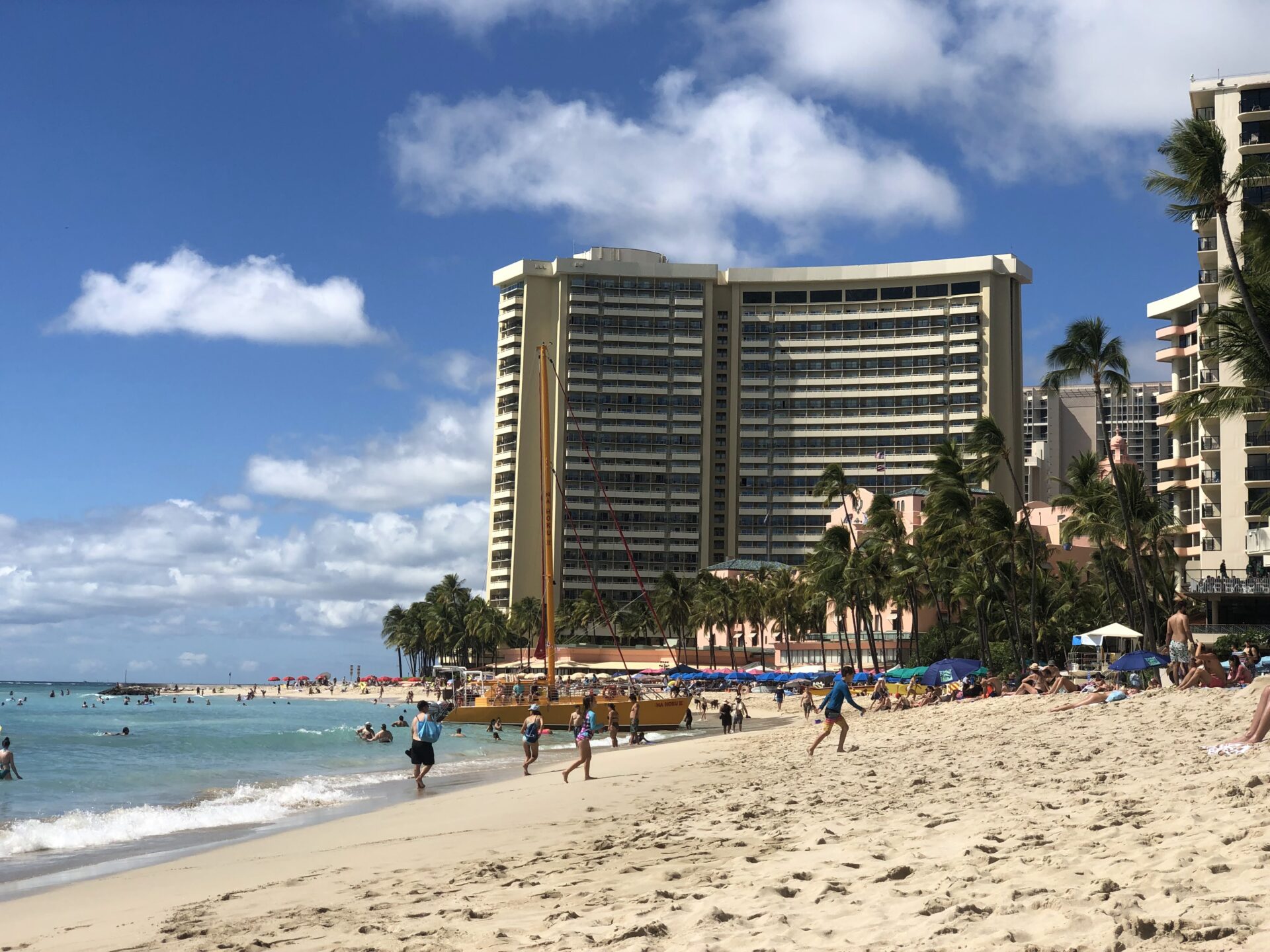 People enjoying their vacation on a beach where there's a hotel next to the ocean