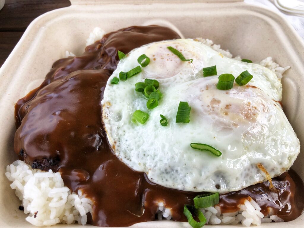 Fried egg on top of a beef patty with gravy and rice