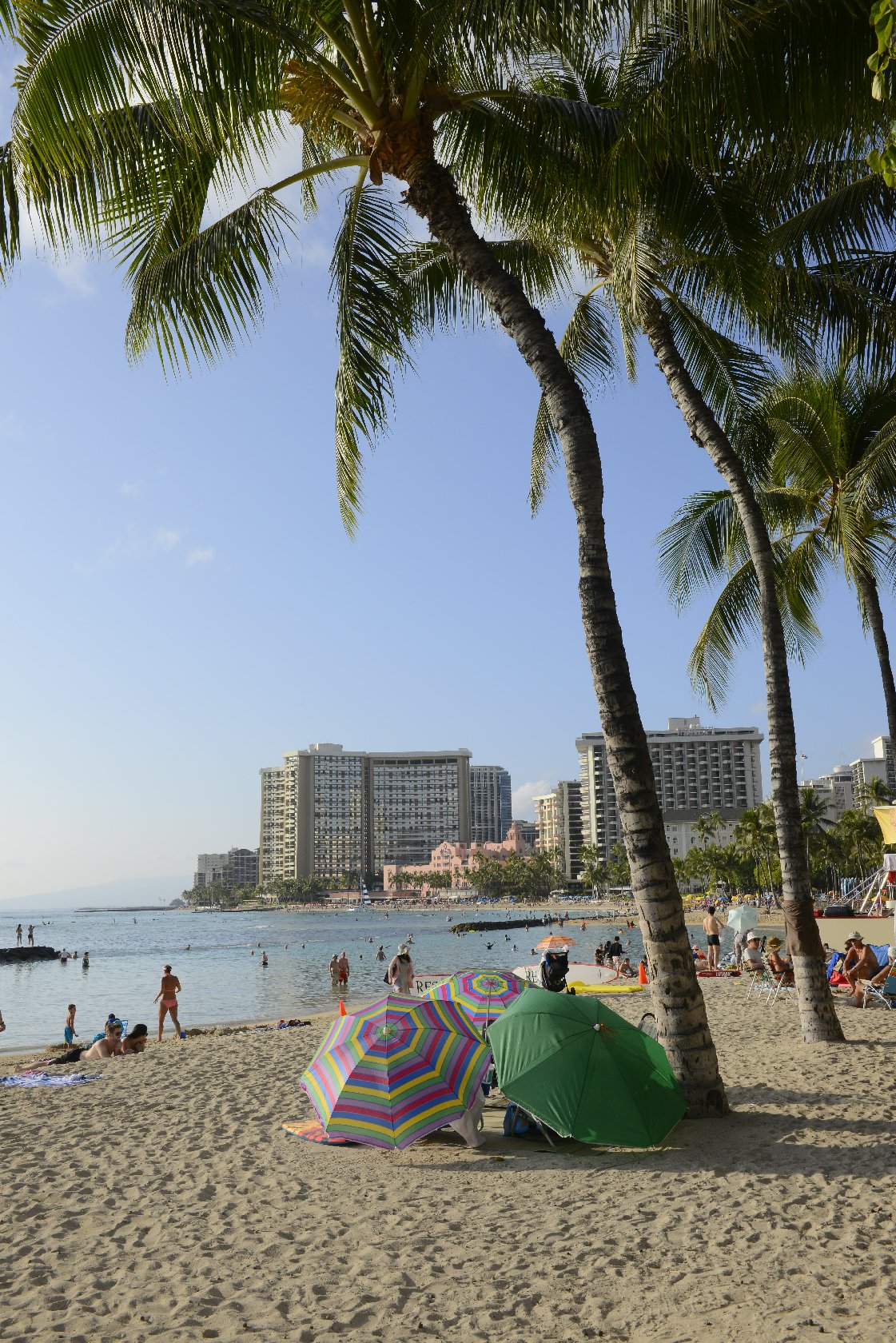 A Oahu Beach Outlook Hotel with vistiors with umbrellas sitting in the sand viewing the beach shore