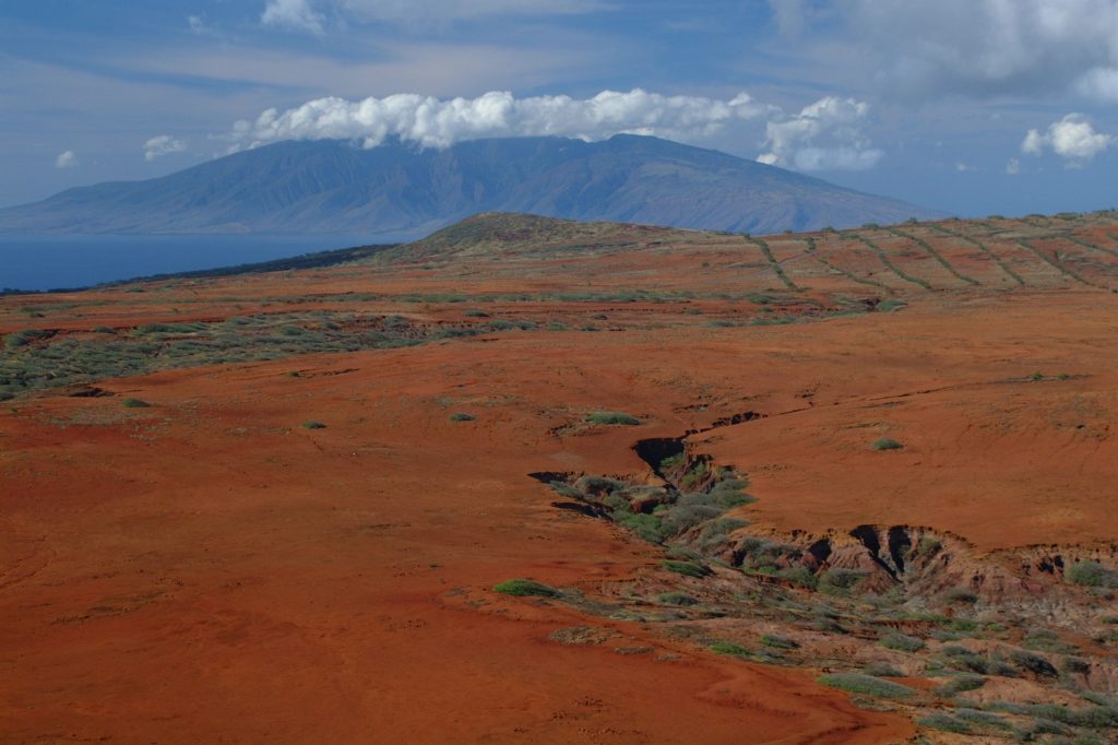 Kahoolawe appeared to be a rugged, barren island with arid terrain and sparse vegetation, with a hawaiian mountain in the background